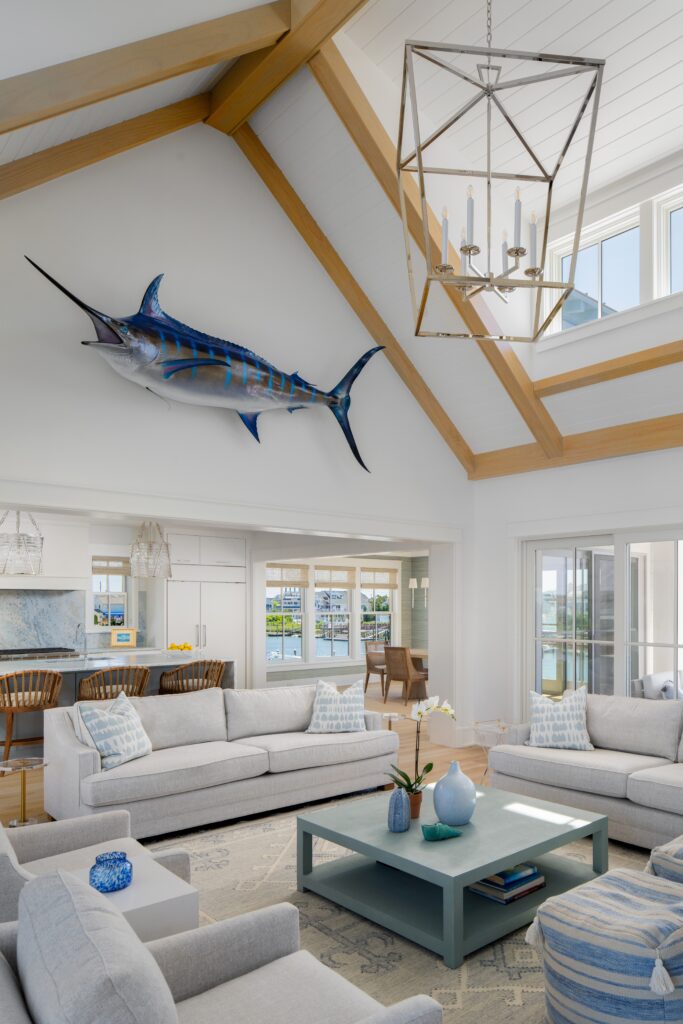 Modern coastal living room with exposed timber ceiling beams, clerestory windows, and a geometric brass pendant fixture.