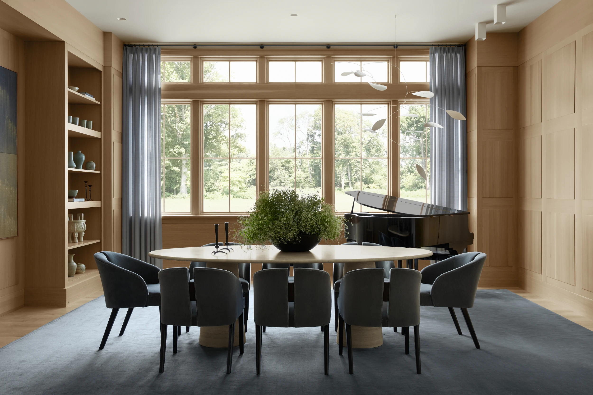 Modern dining room with warm wood millwork, clerestory windows, black dining chairs, and built-in shelving overlooking landscaped grounds.