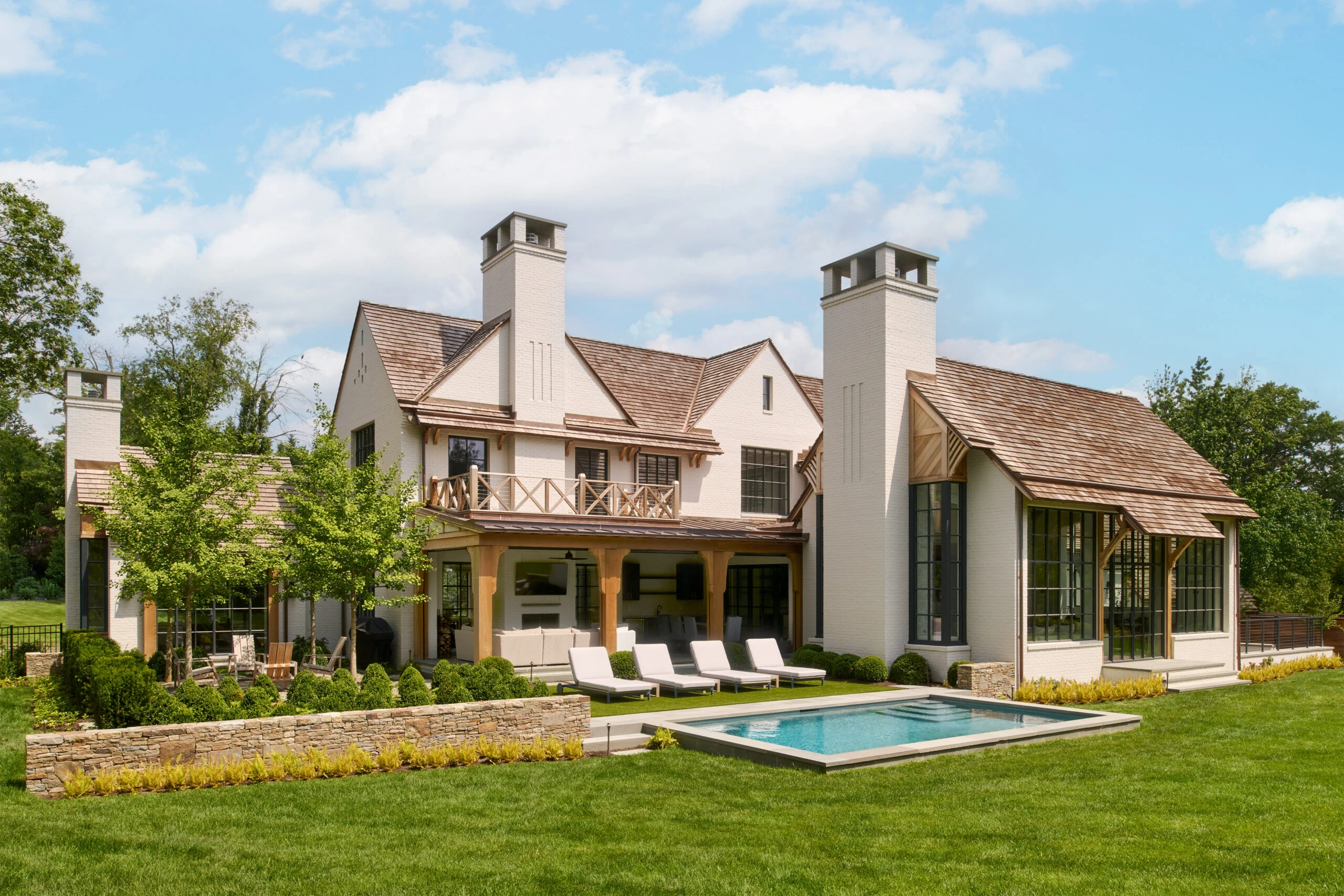 Modern farmhouse exterior with white stucco facade, dual chimneys, stone accents, covered loggia, and pool terrace.