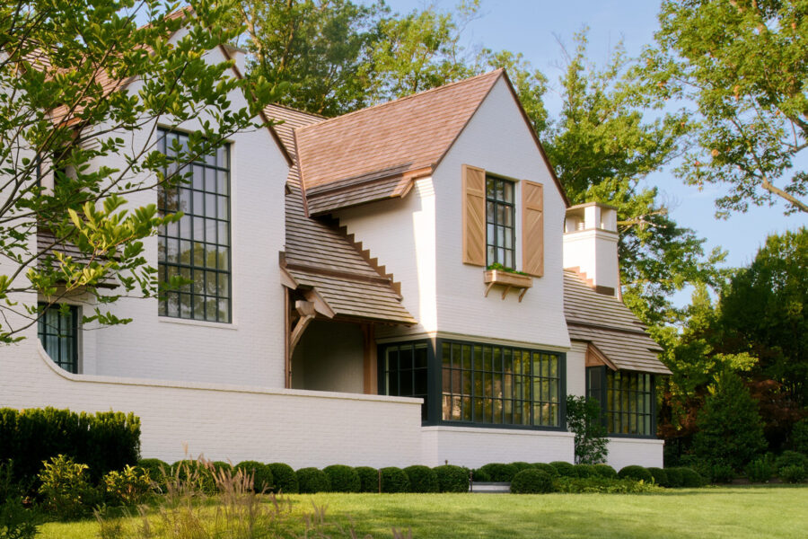 Modern white brick residence with steeply pitched roof, casement windows, and dark-framed glass doors beneath a covered entry.