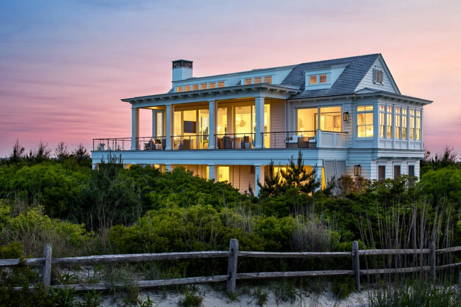 Modern coastal house with light blue clapboard siding, multi-level decks, and clerestory windows at twilight.